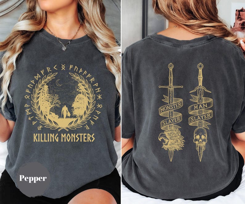 May include: Pepper-colored t-shirt with a gold graphic on the front and back. The front design features a forest scene with the text "KILLING MONSTERS" and runes. The back displays two swords with the text "MONSTER SLAYER" and "MAN SLAYER".