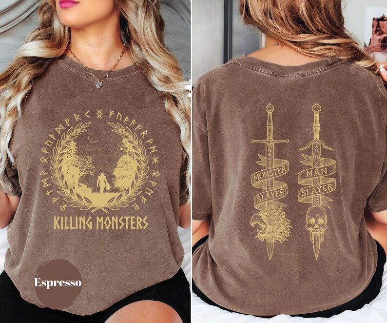 May include: Espresso-colored t-shirt with a gold graphic on the front featuring a forest scene and the text "KILLING MONSTERS." The back displays two swords with the text "MONSTER SLAYER" and "MAN SLAYER."