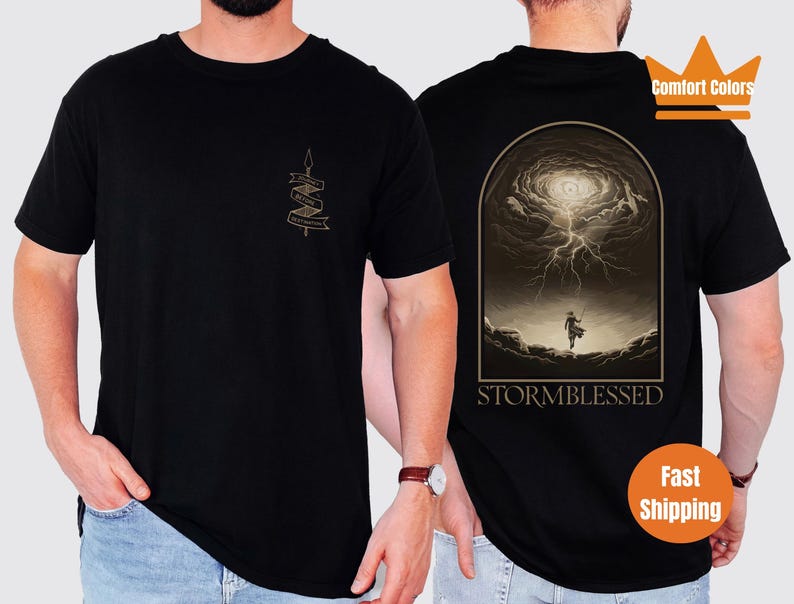Puede incluir: Camiseta negra con un gr&aacute;fico de una persona de pie en un cielo tormentoso con el texto "STORMBLESSED" debajo. La camiseta tiene un peque&ntilde;o gr&aacute;fico en el pecho izquierdo con el texto "Storm Blessed" en una pancarta.
