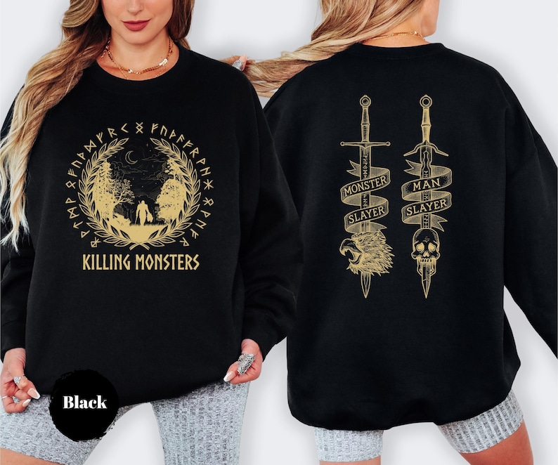 May include: Black sweatshirt with gold-colored graphics. The front features a circular design with the text "KILLING MONSTERS". The back displays two swords with banners that read "MONSTER SLAYER" and "MAN SLAYER".