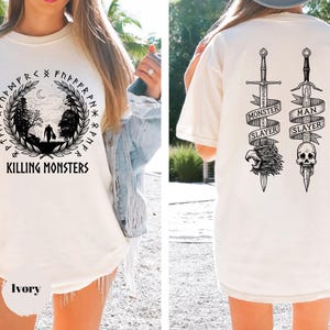 May include: Ivory-colored t-shirt with a front graphic featuring a forest scene, runes, and the text "KILLING MONSTERS." The back displays two swords with banners reading "MONSTER SLAYER" and "MAN SLAYER," along with a skull and eagle graphic.