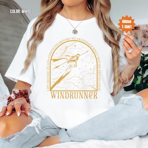 Puede incluir: Camiseta Gildan blanca con una ilustraci&oacute;n dorada de una figura con una lanza. El dise&ntilde;o incluye el texto "LIFE BEFORE DEATH - STRENGTH BEFORE WEAKNESS - JOURNEY BEFORE DESTINATION" y "WINDRUNNER".