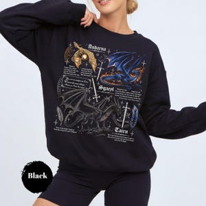 May include: A black long-sleeve sweatshirt featuring a detailed graphic print of three dragons named Andarna, Sgaeyl, and Tairn. The design includes intricate illustrations of the dragons, swords, feathers, and descriptive text blocks in white font.