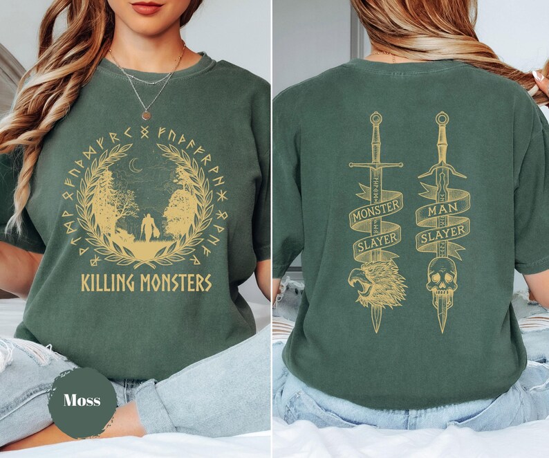 May include: Moss green t-shirt with a gold design featuring the text "KILLING MONSTERS" and a circular illustration. The back displays two swords with the text "MONSTER SLAYER" and "MAN SLAYER".