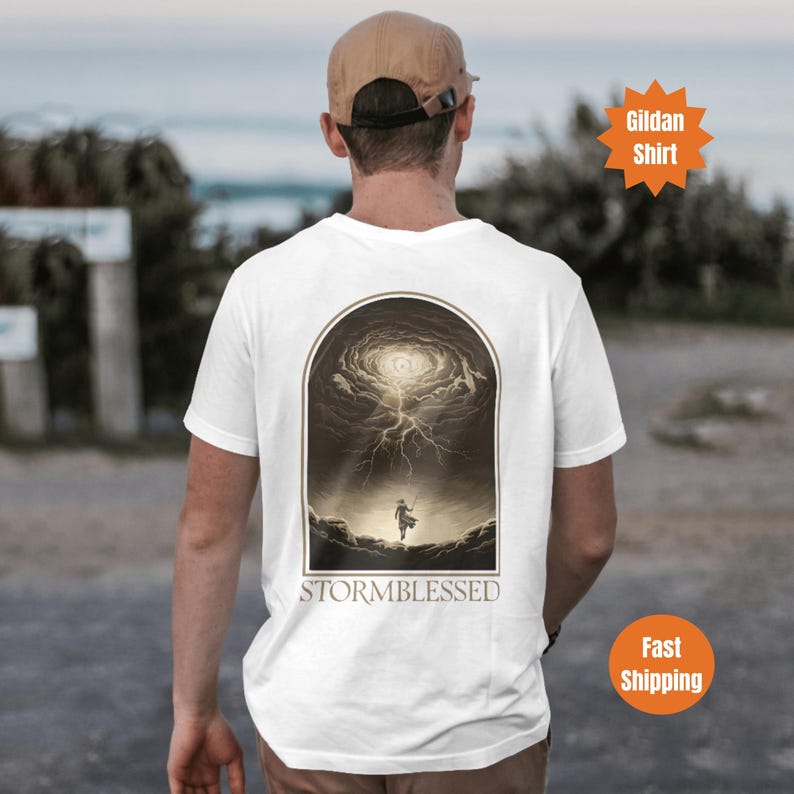 Puede incluir: Camiseta blanca con un gr&aacute;fico de una persona de pie frente a una tormenta giratoria con el texto "STORMBLESSED" impreso debajo.