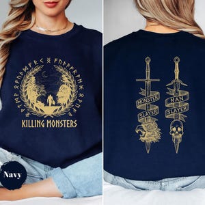 May include: Navy blue sweatshirt with a gold design. The front features a circular design with the text "Killing Monsters". The back has two swords with the text "Monster Slayer" and "Man Slayer".