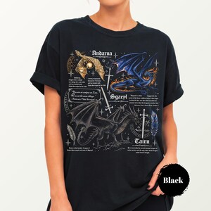 May include: A black t-shirt featuring a graphic print of three dragons labeled Andarna, Sgaeyl, and Tairn. The design includes detailed illustrations of the dragons, swords, feathers, and small text blocks describing each creature, set against a dark background.