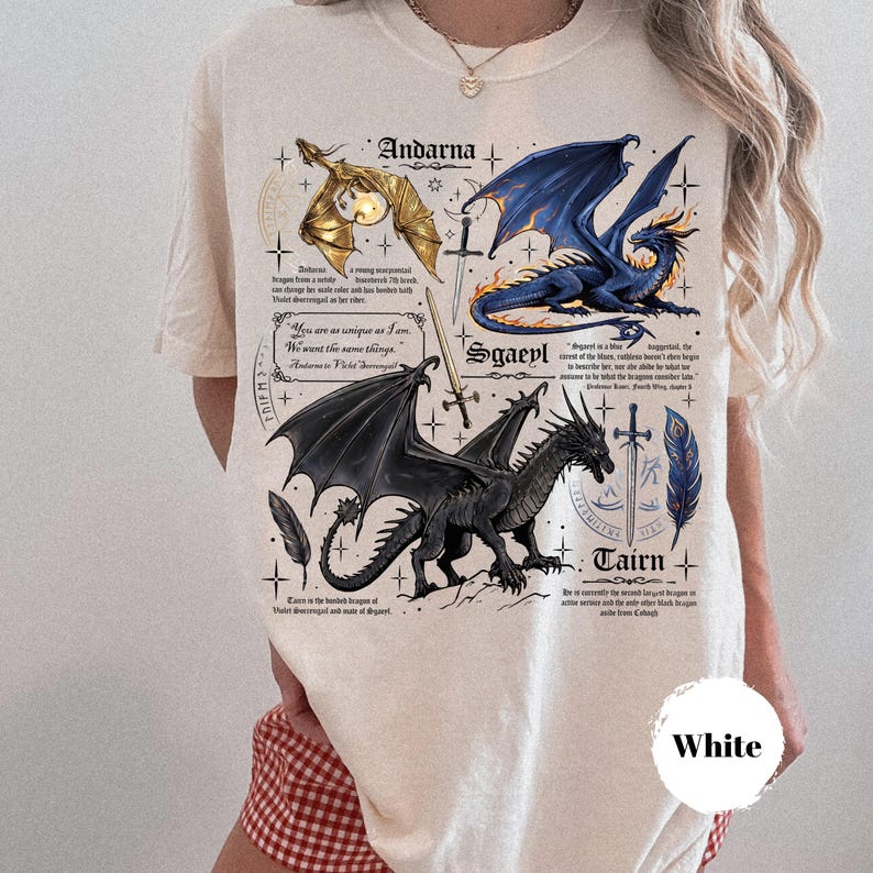 May include: A cream-colored t-shirt featuring a graphic print of three dragons labeled Andarna, Sgaeyl, and Tairn. The design includes illustrations of swords, feathers, and text excerpts. The shirt has short sleeves and a crew neckline.