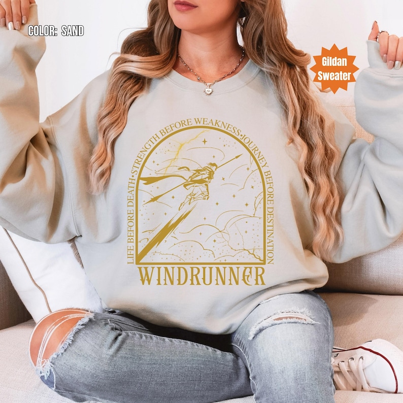 Puede incluir: Sudadera Gildan color arena con una ilustraci&oacute;n dorada de una figura con una lanza, rodeada por el texto "LIFE BEFORE DEATH, STRENGTH BEFORE WEAKNESS, JOURNEY BEFORE DESTINATION" y la palabra "WINDRUNNER".