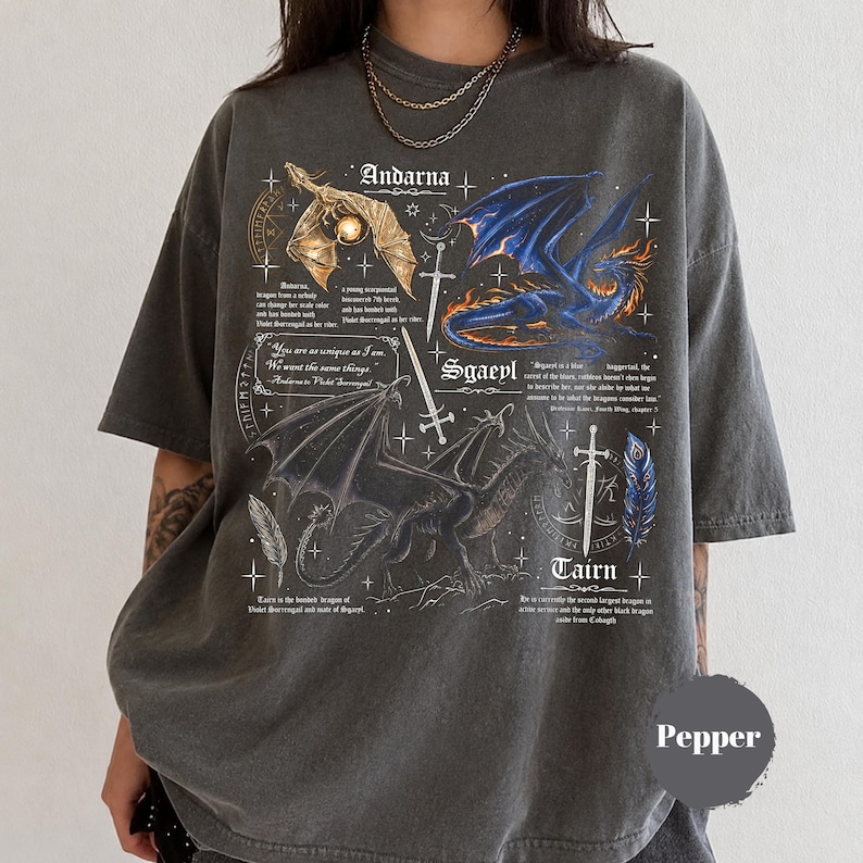 May include: A charcoal gray oversized t-shirt featuring a graphic print of three dragons labeled Andarna, Sgaeyl, and Tairn. The design includes swords, feathers, stars, and text excerpts from the Fourth Wing series. The shirt has a crew neckline.