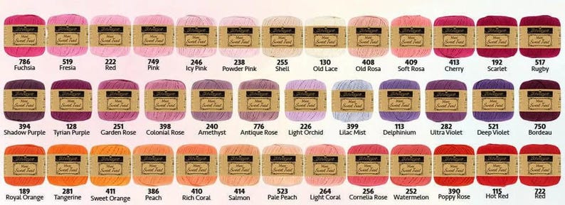 May include: A collection of colorful yarn skeins in various shades of pink, purple, orange, and red. Each skein has a label with a color name and number. The yarn is arranged in rows, showcasing a wide range of hues for crafting projects.