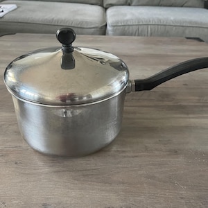 May include: A silver saucepan with a black handle and a lid. The saucepan has a shiny finish and a black knob on the lid.