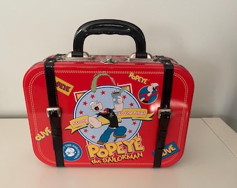 May include: Red metal suitcase with a black handle and black straps. The suitcase has a Popeye cartoon character design with the text "Popeye the Sailorman" and "Strong to the finish".