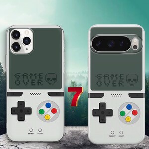 May include: Two smartphone cases featuring a retro handheld gaming console design. The top half is dark gray with the text GAME OVER and a skull icon. The bottom half is white with a black directional pad, four colored buttons, and SELECT START text.