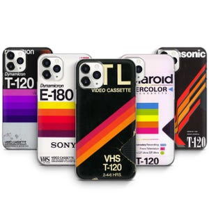 May include: Five different phone cases with retro VHS tape designs. The cases feature black, red, orange, yellow, blue, green, and purple stripes. The text on the cases reads "VHS T-120", "Dynamicron E-180", "VIDEO CASSETTE", "T-120", and "Polaroid Watercolor Cassette".