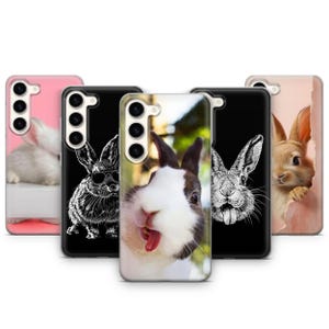 May include: Four phone cases with different designs featuring rabbits. The first case is pink with a white rabbit. The second case is black with a white rabbit wearing sunglasses. The third case is white with a black and white rabbit sticking its tongue out. The fourth case is pink with a brown rabbit peeking out from behind a torn piece of paper.