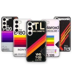 Può includere: Una collezione di custodie per telefoni con design retrò di nastri VHS. Ogni custodia presenta un marchio e un design diversi, tra cui combinazioni di colori vivaci e testo come "VHS T-120" e "Video Cassette". Le custodie sono progettate per uno smartphone.