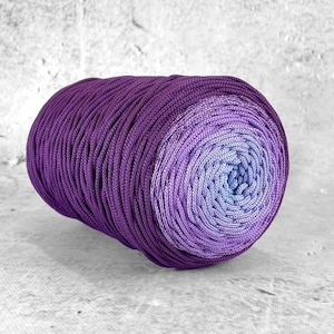 Könnte beinhalten: Eine Rolle lila und lavendelfarbenes Ombre-Garn. Das Garn ist aus einem weichen, glatten Material gefertigt und perfekt zum Häkeln oder Stricken.