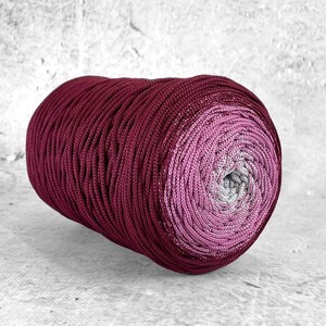Op de afbeelding: Een rol bordeauxrood en roze ombre garen met een zilveren glans. Het garen is opgerold tot een strakke spoel.