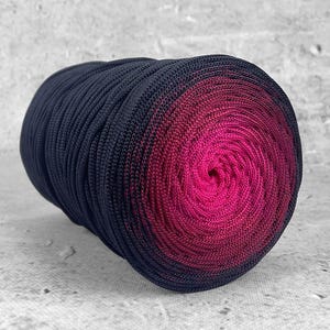 Peut inclure: Une grosse pelote de laine cylindrique avec un dégradé de couleurs. Le fil passe d'un bleu marine profond à un rose fuchsia vif en spirale. Le fil est bien enroulé, ce qui suggère un matériau durable adapté à divers projets de création.