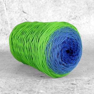 Può includere: Un vivace gomitolo di filato, che passa dal verde brillante al blu intenso. Il filato è avvolto strettamente, creando una superficie strutturata. Ideale per progetti di maglia o uncinetto.