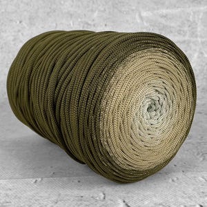 Peut inclure: Une bobine de fil vert olive, passant à une teinte beige plus claire au centre. Le fil est torsadé serré, créant une surface texturée. Idéal pour divers projets de création.