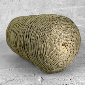 Op de afbeelding: Een grote, olijfgroene bol garen met een strak geweven, getextureerd oppervlak. Het garen heeft een effen kleur, met een lichte gradiënt naar het midden. Geschikt voor diverse handwerkprojecten, zoals breien of haken.