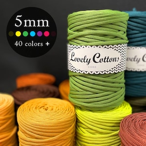 Op de afbeelding: Een verzameling kleurrijke 5 mm Lovely Cottons-garenspoelen. De afbeelding toont verschillende kleuren, waaronder groen, geel, oranje en blauwgroen. Het label op de groene spoel luidt "Lovely Cottons CORD". De afbeelding bevat ook een afbeelding met 40+ kleuren.