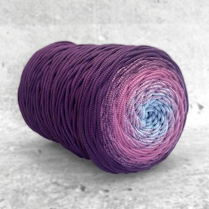 Könnte beinhalten: Ein Garnknäuel in Lila-, Rosa- und Blautönen. Das Garn ist eng gewickelt, mit einem Farbverlauf von einem tiefvioletten Äußeren zu einem hellblauen Zentrum. Das Garn eignet sich für Strick- und Häkelprojekte.