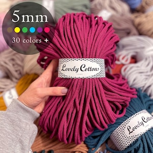 Könnte beinhalten: Ein Bündel leuchtend magentafarbenes 5 mm Lovely Cottons-Kordel. Das Etikett lautet "Lovely Cottons CORD". Das Bild zeigt auch eine Farbpalette mit über 30 Farben. Weitere Kordel-Bündel in verschiedenen Farben sind im Hintergrund zu sehen.