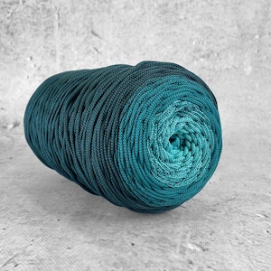 Könnte beinhalten: Eine Rolle teal- und dunkelgrünes Ombre-Garn. Das Garn ist zu einer engen Spule gewickelt.