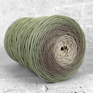 Puede incluir: Un ovillo de hilo en tonos verdes, marrones y beige. El hilo presenta un degradado de color, pasando de verde claro a marrón oscuro en el centro. Ideal para tejer o hacer ganchillo.