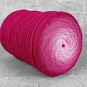 Op de afbeelding: Een grote bol garen in roze tinten, van diep magenta tot lichtroze in het midden. Het garen is strak gewikkeld en ziet er glad uit, geschikt om te breien of te haken. Het garen wordt gemeten in gram.