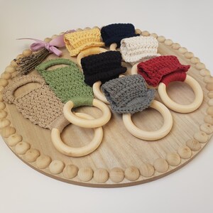 May include: A set of eight crocheted teethers attached to wooden rings. The teethers are in various colors, including beige, green, red, black, and gray.