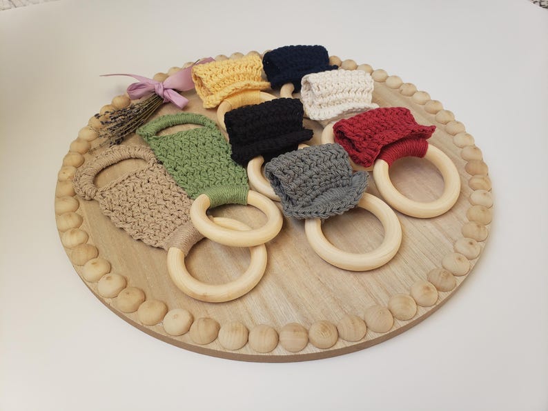 May include: A set of eight crocheted teethers attached to wooden rings. The teethers are in various colors, including beige, green, red, black, and gray.