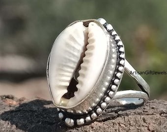 May include: A silver ring with a white cowrie shell design. The ring has a beaded edge and a simple band.