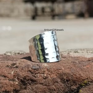 May include: A silver hammered ring with a wide band. The ring is made of metal and has a textured surface.
