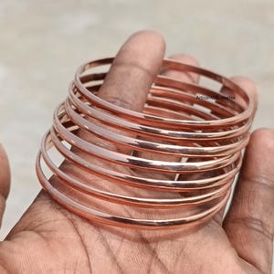 Op de afbeelding: Een set van tien roségouden armbanden die op elkaar gestapeld zijn. De armbanden zijn dun en hebben een gladde, gepolijste afwerking.