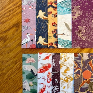 May include: A collection of decorative bookmarks with Japanese-inspired designs. The bookmarks feature various patterns, including koi fish, cranes, lotus flowers, and dragons. The color palette includes shades of purple, blue, gold, and red.