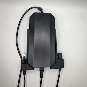 Könnte beinhalten: Ein schwarzes elektronisches Gerät mit dem Aufdruck "MOBILE" auf der Vorderseite. Das Gerät hat mehrere Anschlüsse und ist mit mehreren schwarzen Kabeln verbunden. Es ist an einer weißen Wand montiert.