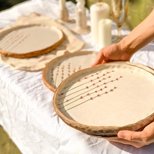 May include: A set of beige ceramic plates with a brown rim and a floral design. The plates are on a white tablecloth, with candles and lavender in the background. The plates are being held by a person.