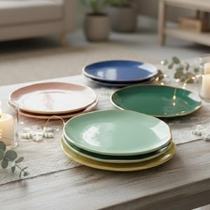Può includere: Una collezione di piatti in ceramica colorati nei toni del rosa, blu, verde e giallo. Ogni piatto ha un bordo dorato. I piatti sono impilati e disposti su un tavolo chiaro, ideali per servire i pasti.