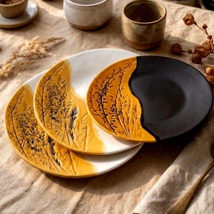 Pode incluir: Um conjunto de pratos de cerâmica com um design inspirado na natureza. Os pratos apresentam uma base branca com detalhes em amarelo e preto. A secção amarela apresenta um padrão botânico detalhado em relevo. Parte de um conjunto de loiça.