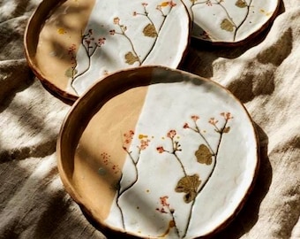 Può includere: Tre piatti rotondi in ceramica con bordi irregolari modellati a mano. Ogni piatto presenta un design bicolore con una smaltatura bianca liscia e lucida su una metà e una finitura in argilla naturale non smaltata sull'altra metà.