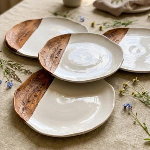 Może przedstawiać: Zestaw trzech okrągłych talerzy ceramicznych o nieregularnych, organicznych krawędziach. Każdy talerz ma gładką, błyszczącą białą powierzchnię z jednej strony oraz teksturowany, ciemnobrązowy wzór słojów drewna z botanicznym odciskiem z drugiej.