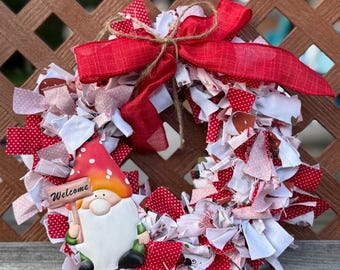 May include: A handmade fabric wreath with red and white polka dot and solid fabric strips. A gnome figure with a red and white mushroom cap holds a "Welcome" sign. A large red bow is tied at the top.