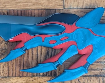 Peut inclure: Une épée fantastique avec une lame incurvée bleu foncé et une garde détaillée. La garde présente un design complexe avec des accents rouges et bleus. La longueur totale de l'épée est d'environ 61 cm.