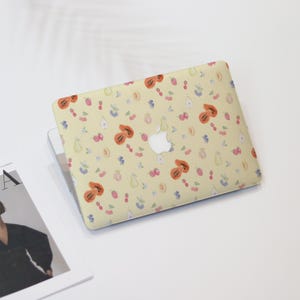 May include: A yellow laptop skin with a pattern of fruit and berries. The fruit includes papaya, pears, and peaches. The berries are red and blue.
