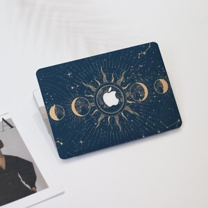 May include: A navy blue laptop case featuring a celestial design with a sun, moon phases, and stars. The Apple logo is centered within the sun. The case has a gold and white color scheme.