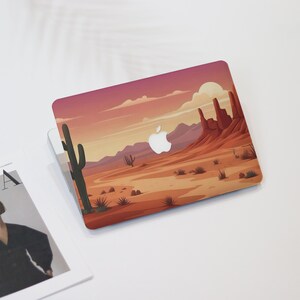May include: A laptop case featuring a desert landscape design. The case showcases a sunset with red and orange hues, a cactus, and rock formations. The Apple logo is visible. The design evokes a southwestern theme.